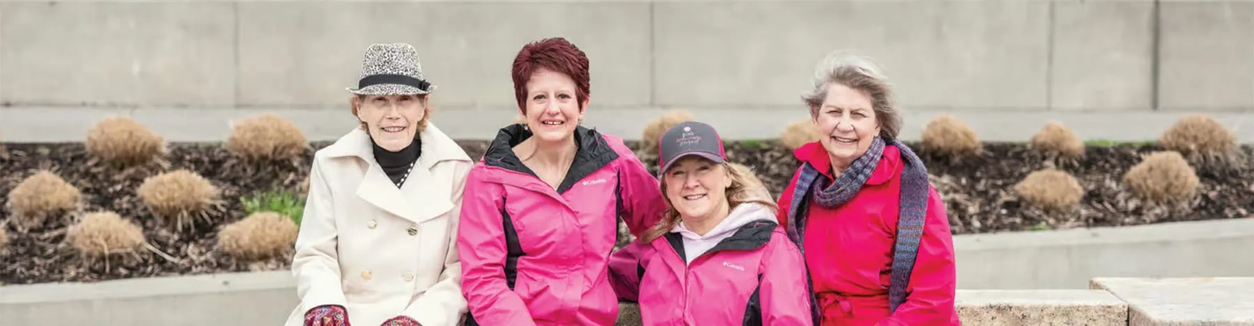 Four Pink Lemonade Project supporters in pink jackets, seated together outdoors at an event