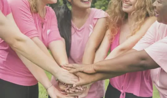 Women in pink T-shirts stacking their hands together in the middle of a circle