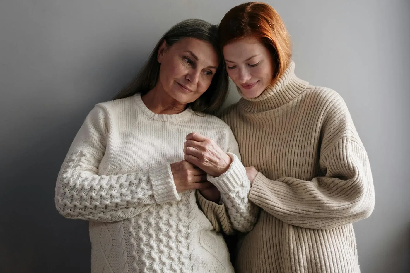 An older woman and a younger woman holding hands, leaning together